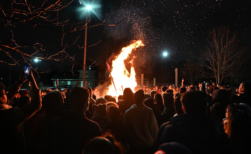 Attendees gather around a pyre. Some throw wood, coconut and popcorn into the fire, meant to wash away evil.