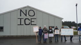 A group of local pilots and organizers stand by a hangar they have painted with “NO ICE”. “We are one human family,” a sign in Spanish held by one demonstrator reads.