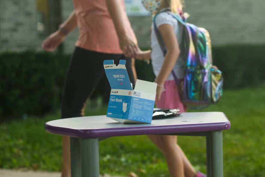 A parent and child hold hands walking past a table with face masks headed into Schoolcraft Elementary in Schoolcraft, Mich., on Aug. 30.