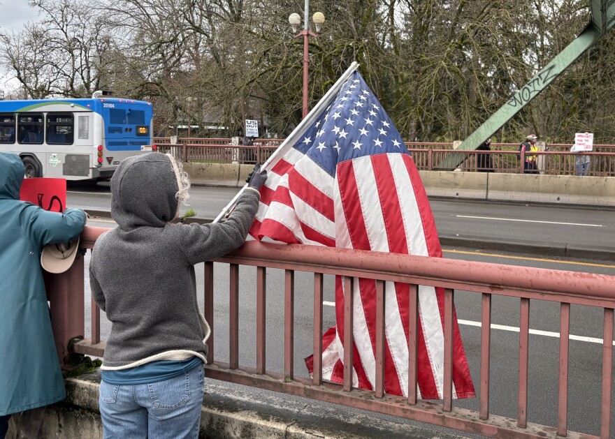 Barbara Stebbins waves an American flag over the guard rails of the Ferry Street Bridge on Dec. 18, 2025.
