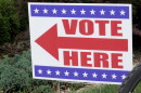A red white and blue sign with an arrow that says "vote here"