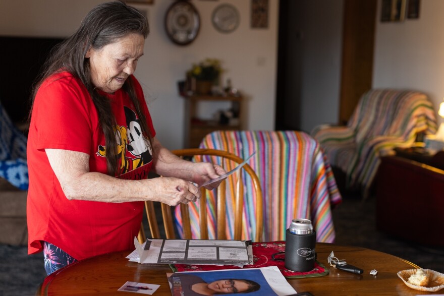 A woman stands in front of a wooden kitchen table, sorting through photos.