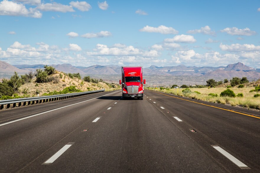 A red semi truck drives down a highway.
