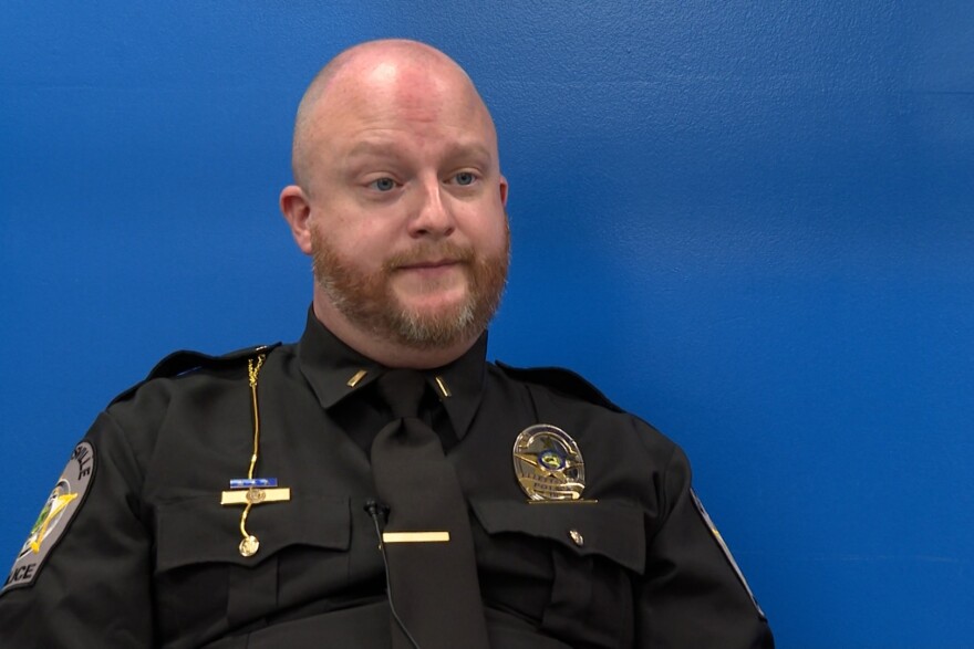 Detective Lieutenant Zachary Michael sits in front of a blue background. He is a bald man wearing a black police officer's uniform.