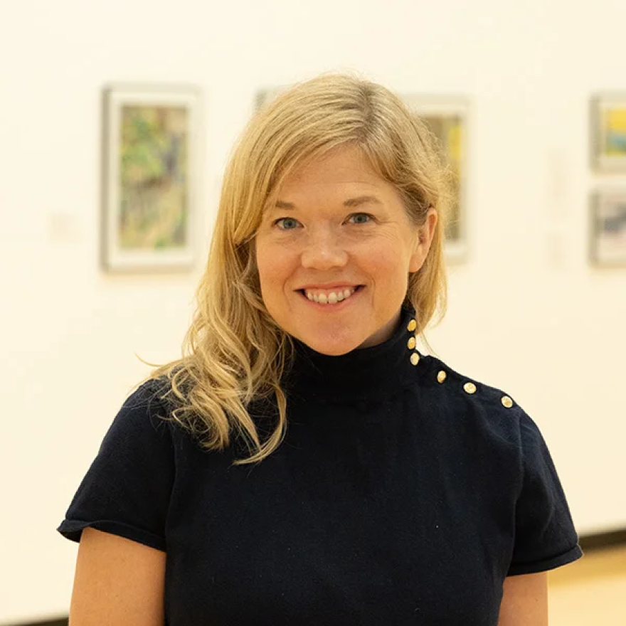 An upper half picture of a woman with blonde hair and a black shirt, smiling and facing forward