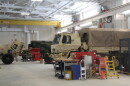Military vehicles are parked for servicing inside of a National Guard field maintenance shop.