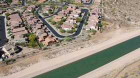 A blue-green canal carries water past a neat cluster of multi-story homes