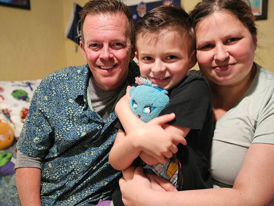 Darren Chase (left) and Erin Booth (right) sit with their 9-year-old son Landon in his bedroom. The family has been on a health journey that began in 2021 when Landon was diagnosed with leukemia. He beat his cancer in 2023, but Landon has been on a long road to recovery made harder because his insurance, through the Florida Healthy Kids Corporation, won't cover more than 24 therapy sessions. His doctors recommend occupational therapy, speech therapy, and physical therapy.