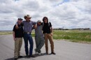 Four young men stand with their arms around each other in the middle of a street. 