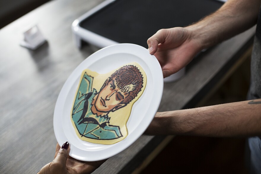 Daniel Drake presents a finished pancake to St. Louis Public Radio reporter Marissanne Lewis-Thompson.