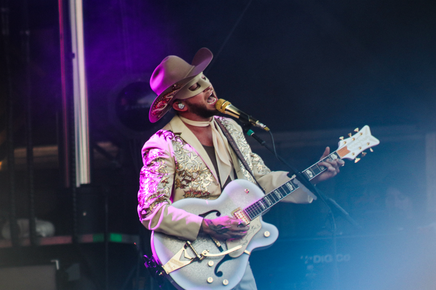 Orville Peck performing in a beige suit with with his lone ranger mask at the Hinterland music festival.
