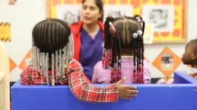 two children sit next to each other and engage in a visual learning activity with their professor