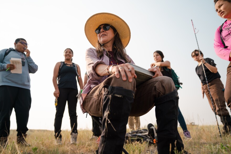 Eisenberg sits on a camp chair surrounded by the fellows and field crew. The team, led by Eisenberg and Fox, will collect grass samples, take transect measurements and analyze seed samples.