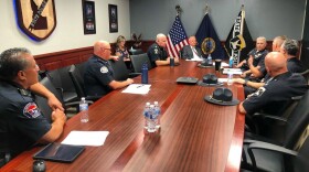 Uniformed police officers sit around rectangular conference table, talking to the governor of Idaho.