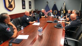 Uniformed police officers sit around rectangular conference table, talking to the governor of Idaho. 