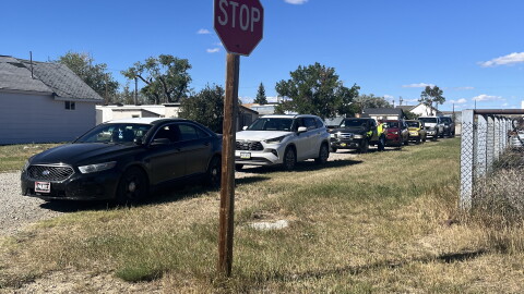 A line of cars waiting to receive food in Rock River. A stop sign in the foreground.