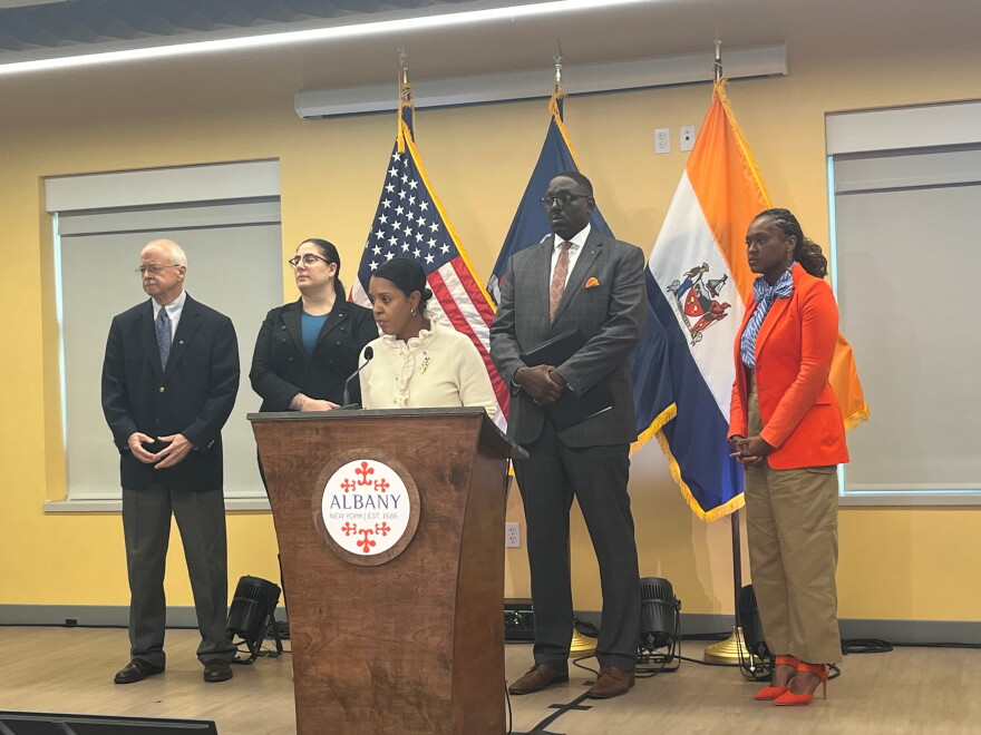 Mayor Dorcey Applyrs is standing behind a lectern with the city seal. She's flanked by two people in dress clothes on each side. 