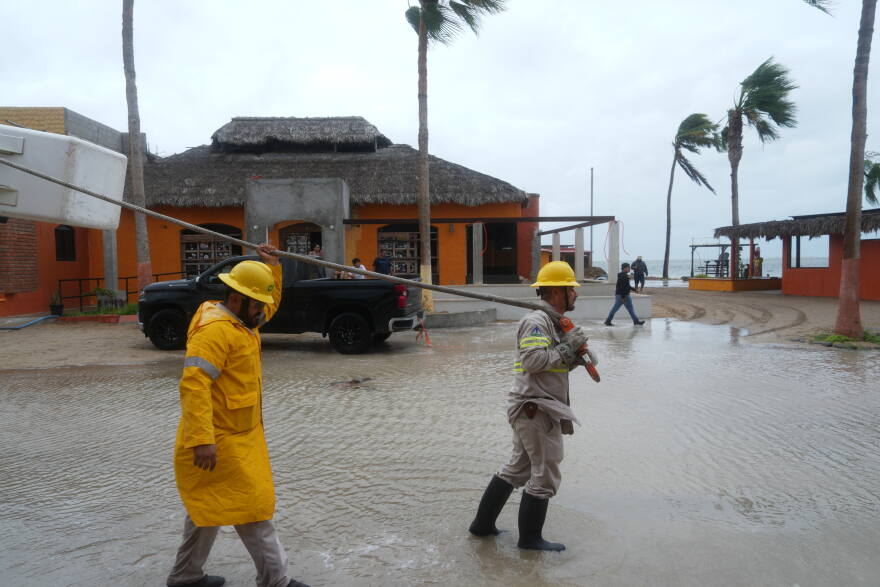 Workers in reflective jackets and rain boots pull a boat to shore in floodwaters in Mexico after Hurricane Polo blew through Baja California.