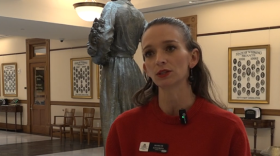 A woman wearing a red sweater and a name tag speaks while looking just to the side of the camera.