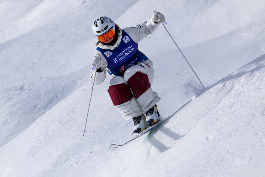 A woman wearing a helmet and a ski bib charges down a snowy slope on skis.