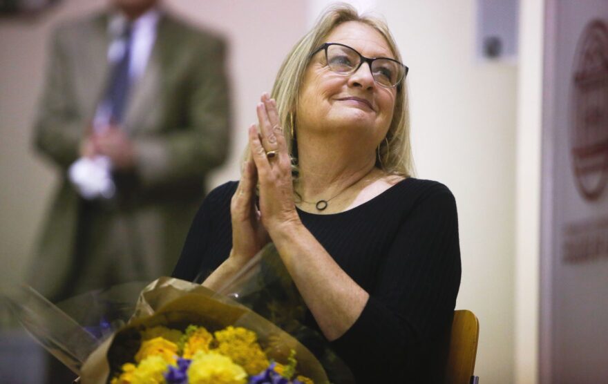 Petersen sat on a chair next to the lectern. She pressed her hands together, as though she were praying. Her eyes wrinkled and a small smile escaped her lips. (Chris Day/WUFT News)