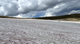 Two researchers stand on a vast ice patch in Wyoming’s Beartooth Mountains beneath large, dark clouds.