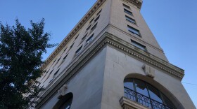 Picture of the Flatiron building, a seven-story building in downtown Asheville with some older architectural trappings and window designs. A tree borders the left side.