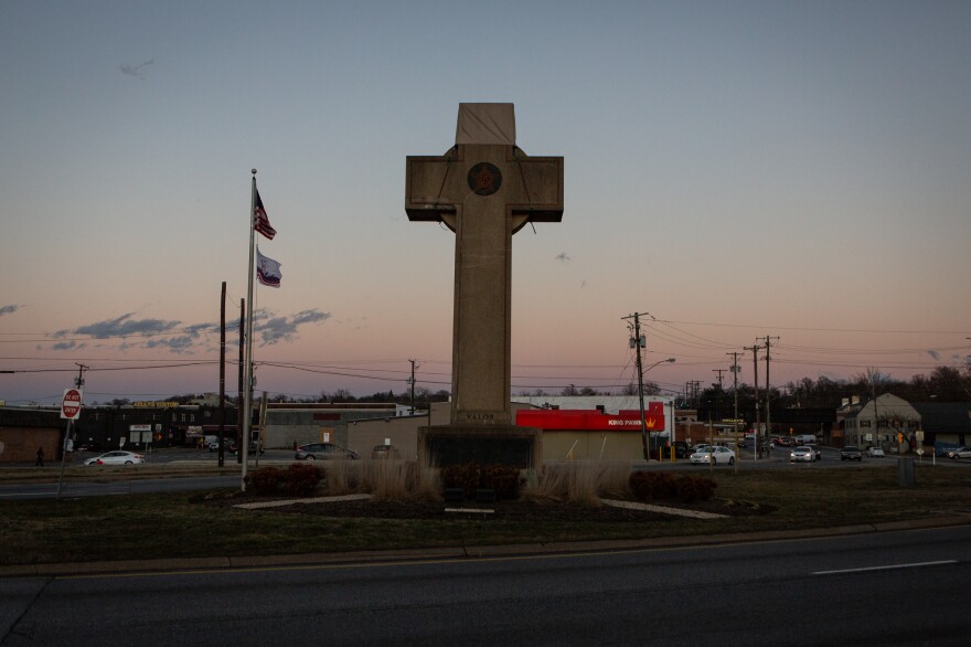 The cross sits in the median at a busy five-way intersection.