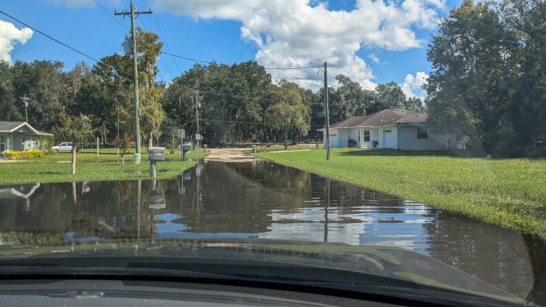 Several inches of floodwater is visible on a street in this image, captured from inside a car, through the windshield.
