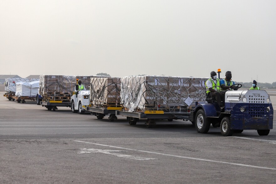 Airport workers transport the 600,000 donated vaccines in Ghana. The president is getting a dose — and so are health workers.