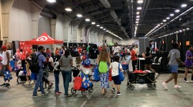 lots of families and children in a lighted warehouse, many pulling filled wagons or with large colored bags in hand or over shoulders