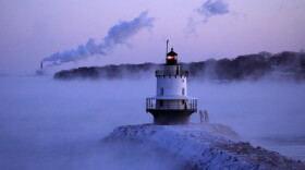 Spring Point Ledge Light is surrounded by arctic sea smoke while emissions from the Wyman Power plant, background, are blown horizontal by the fierce wind, Saturday, Feb. 4, 2023, in South Portland, Maine. The morning temperature was about -10 degrees Fahrenheit. (AP Photo/Robert F. Bukaty)