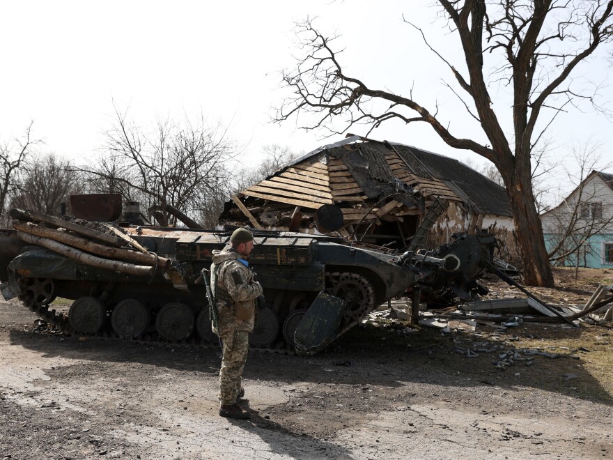 A Ukrainian soldier stands in front of a destroyed Russian armored personnel carrier in a village on the frontline of the northern part of the Kyiv region on Monday. Russia says its troops are starting to withdraw from Kyiv, thought the Pentagon believes they will likely be deployed elsewhere in Ukraine.