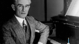 Maurice Ravel, seated at a piano, with a birthday hat