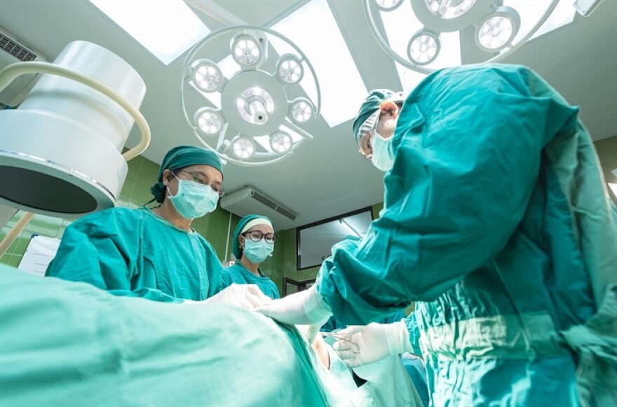 A doctor and nurses work on a patient in an operating room, wearing green scrubs