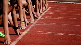 We see hands perched on a starting line as athletes prepare for a running competition