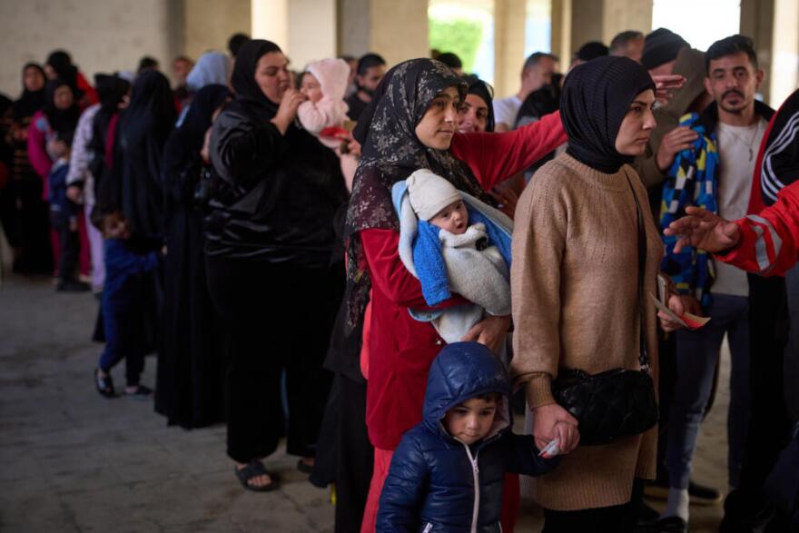 Displaced men and women with their children from Beirut's southern suburbs, wait to receive donated food rations inside a school converted into a shelter in Beirut, Lebanon, Friday, March 27, 2026. (Emilio Morenatti/AP)