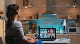 Woman falling asleep during video conference on laptop working from home late at night in the kitchen.