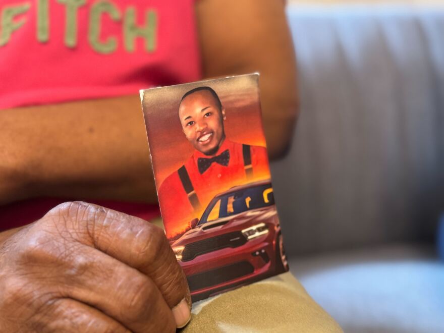 A hand holding up a photo of a man with a car.