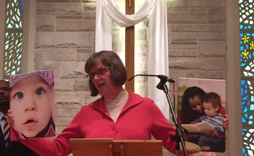 Woman at church podium holding a photo of children in each hand.