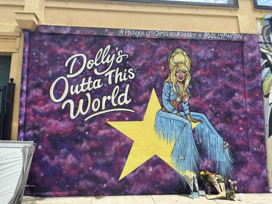 a mural of country singer Dolly Parton sitting on a yellow star with the words "Dolly's Outta This World."