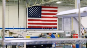 Large American flag is displayed along the back wall of a manufacturing room as an employee stands next to a desk