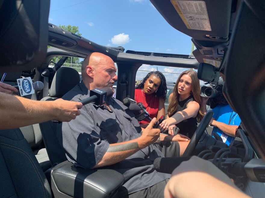 A balding man speaks with reporters while seated in a vehicle
