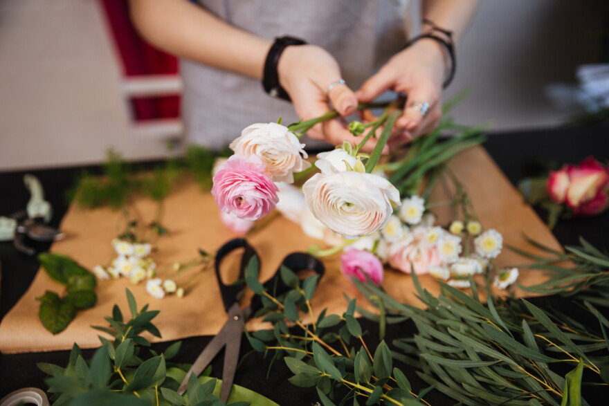 Closeup of hands of young woman florist creating bouquet of pink roses on the table