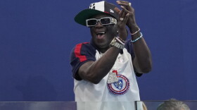 Flavor Flav cheers the U.S. team during a women's water polo Group B preliminary match between the United States and France, at the 2024 Summer Olympics, Friday, Aug. 2, 2024, in Saint-Denis, France. (AP Photo/Luca Bruno)