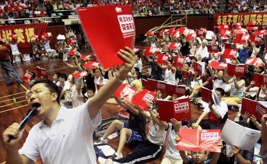 Li Yang teaches English to several thousand students attending a class at a stadium in Guangzhou, China, in 2004. His "Crazy English" technique — based on learning through shouting — draws huge crowds. In interviews, he has admitted physically attacking his wife.