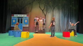 People standing on a green and yellow stage with red, blue and yellow blocks around the floor.