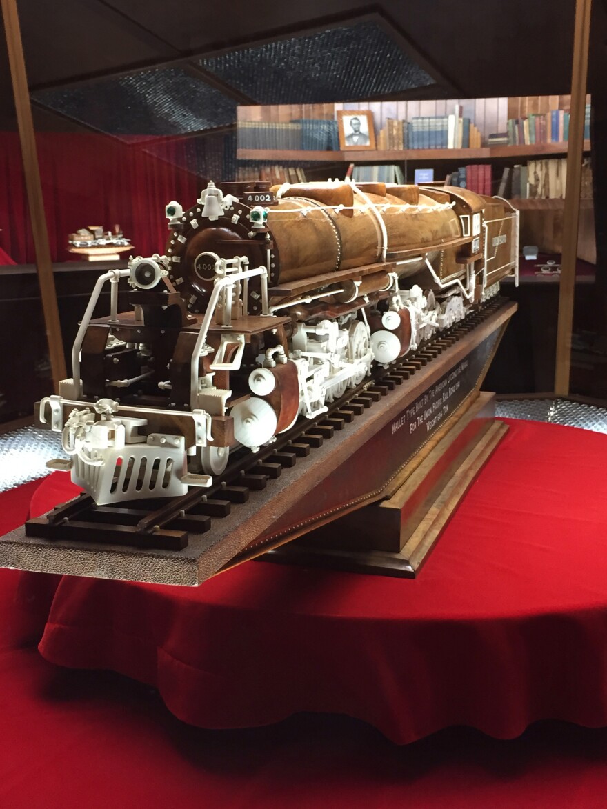 A wood carving of a steam engine train from the 1940s on view in a museum case.