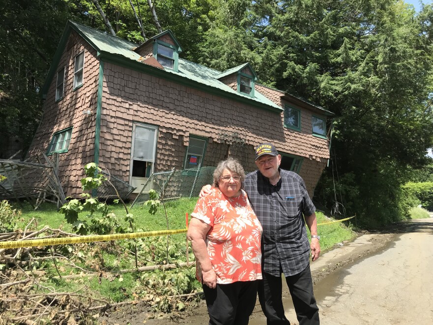 Two people standing in front of a partially collapsed house