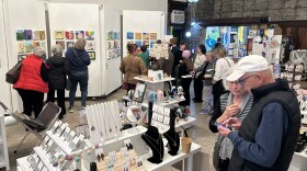People standing in an art gallery featuring paintings, jewelry, and gift cards.